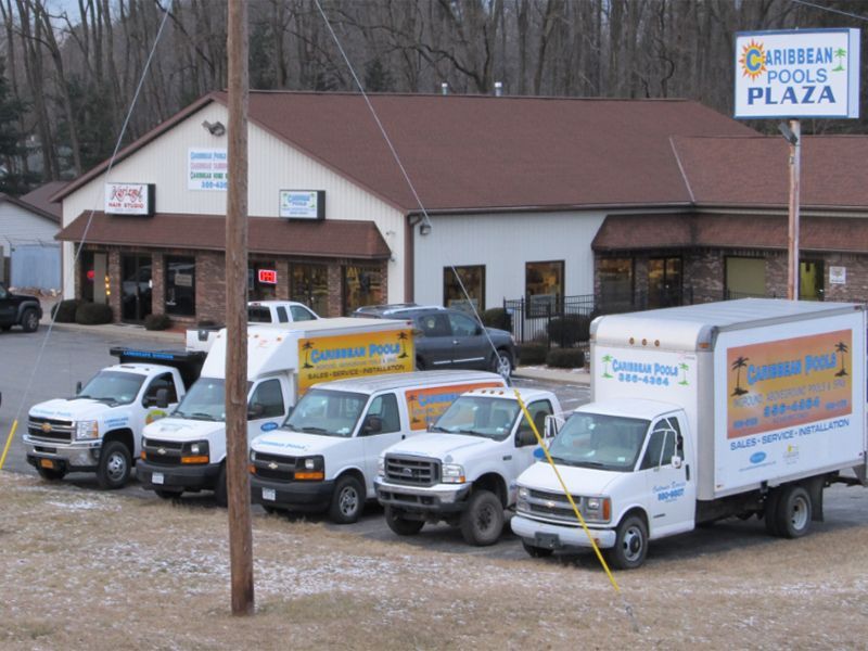 Several white service vehicles parked in front of Caribbean Pools Plaza, with building in the background and a sign.