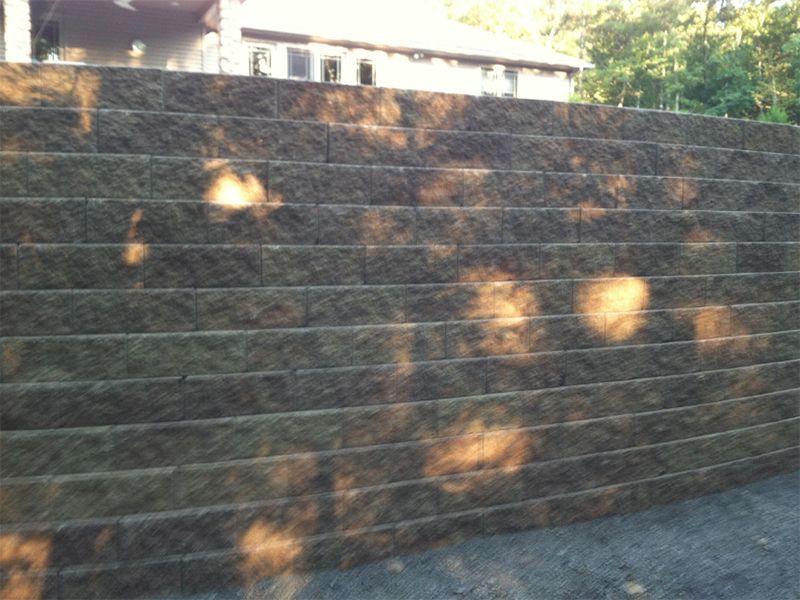 Retaining wall made of dark stone blocks, tiered, with sunlight dappling its surface.