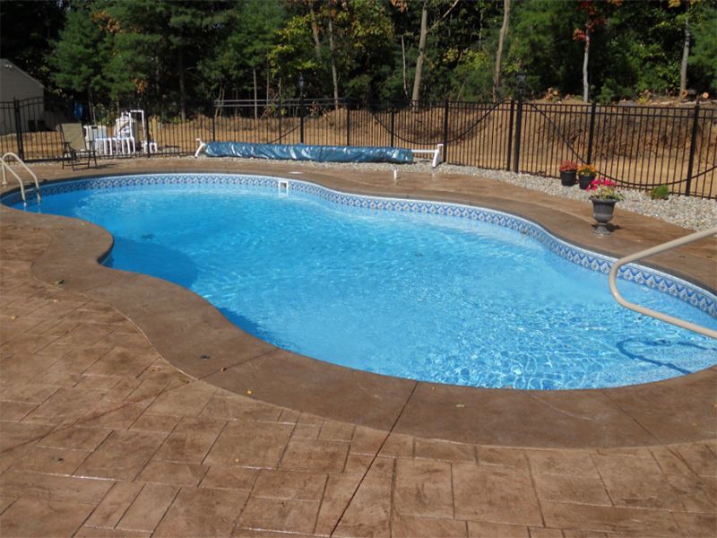 An irregularly shaped blue swimming pool surrounded by brown concrete and a black fence.