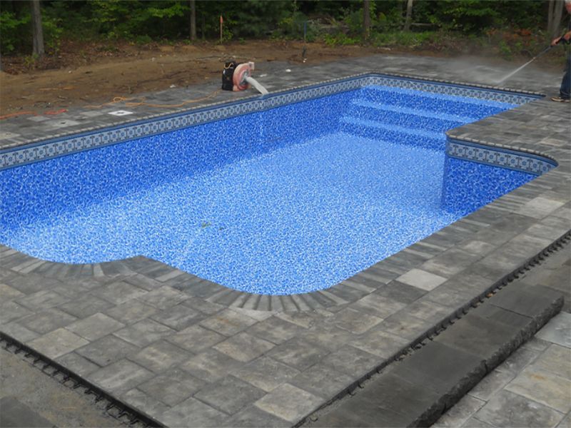 A rectangular in-ground pool with blue tile interior and gray brick coping, steps, and surrounding patio.