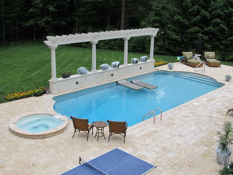 Outdoor pool with a pergola, hot tub, and patio furniture. Blue water and light-colored stone surround.