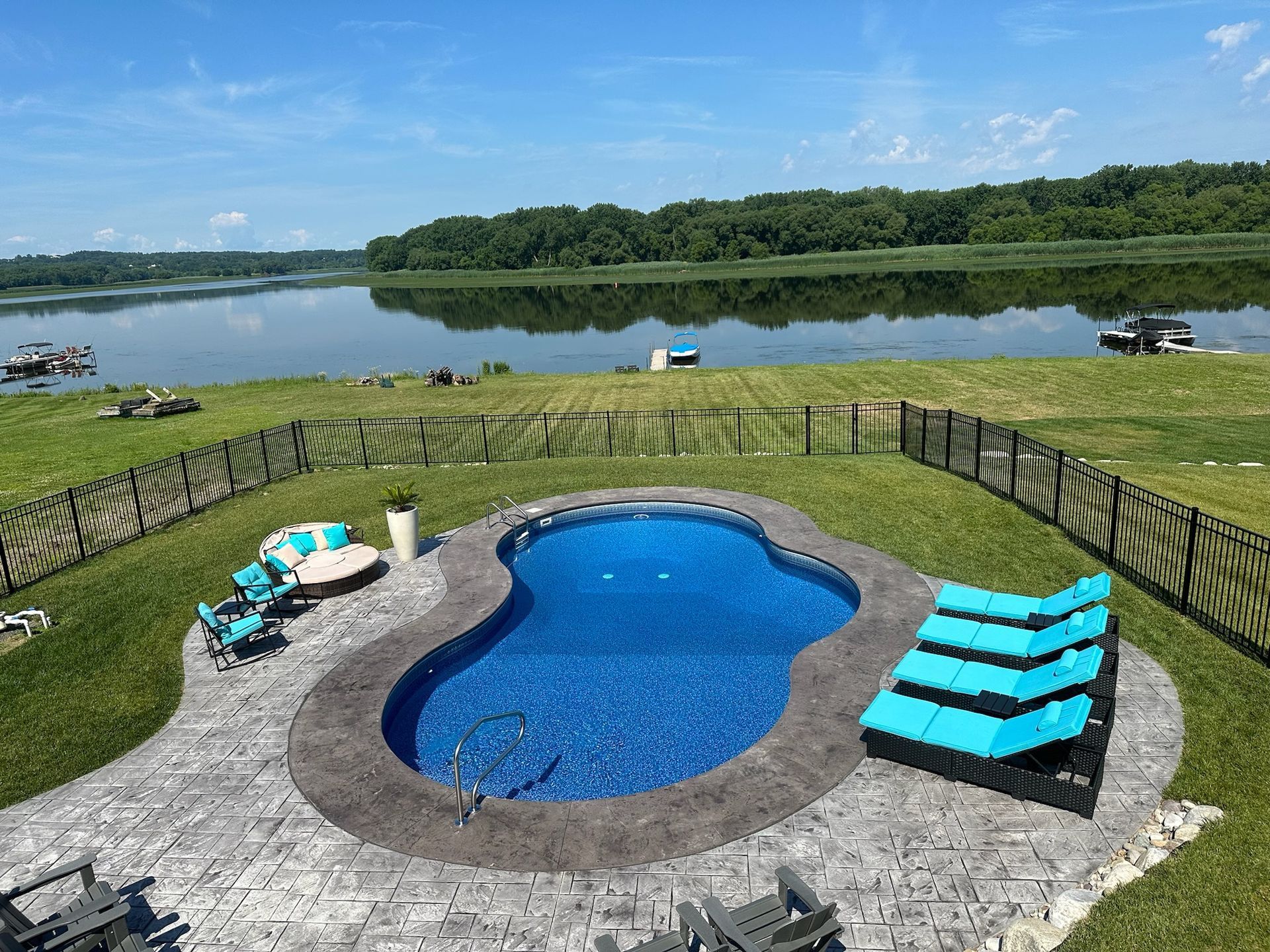 Pool with blue water and patio furniture overlooking a lake.