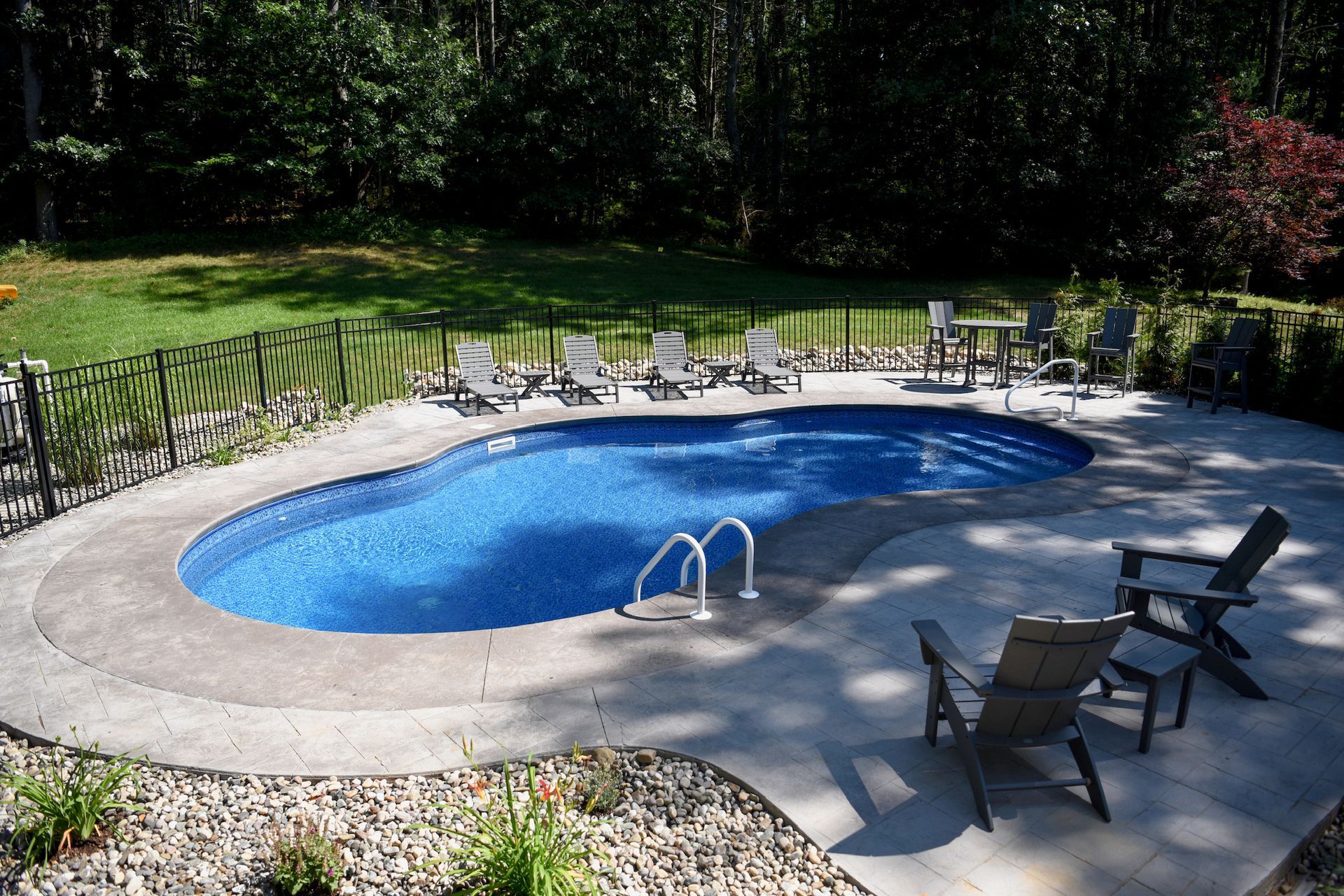 Swimming pool with lounge chairs on a sunny, landscaped patio with surrounding trees.