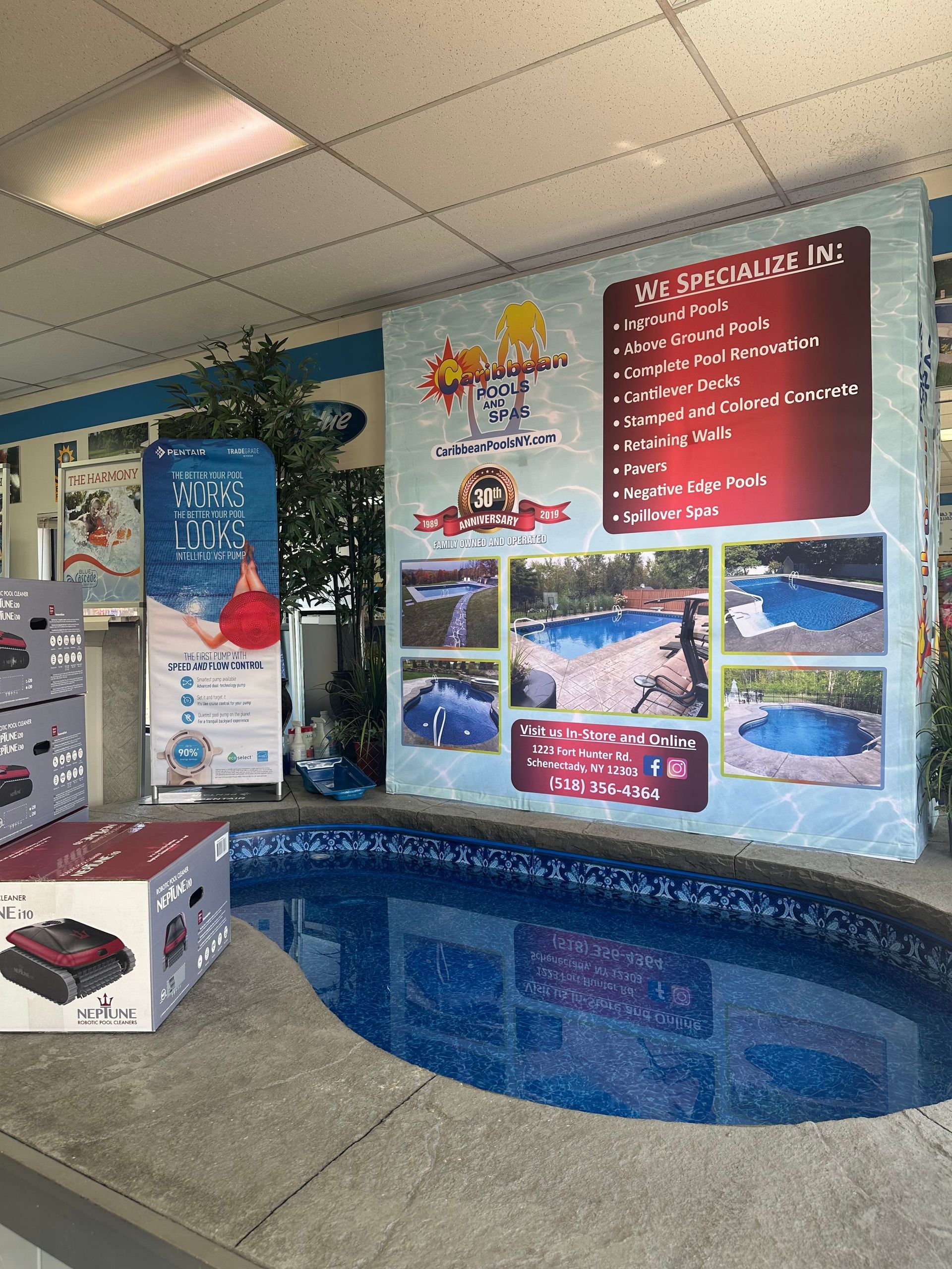 Indoor pool display with marketing material. Blue water, rock border, and signs promoting pool sales.