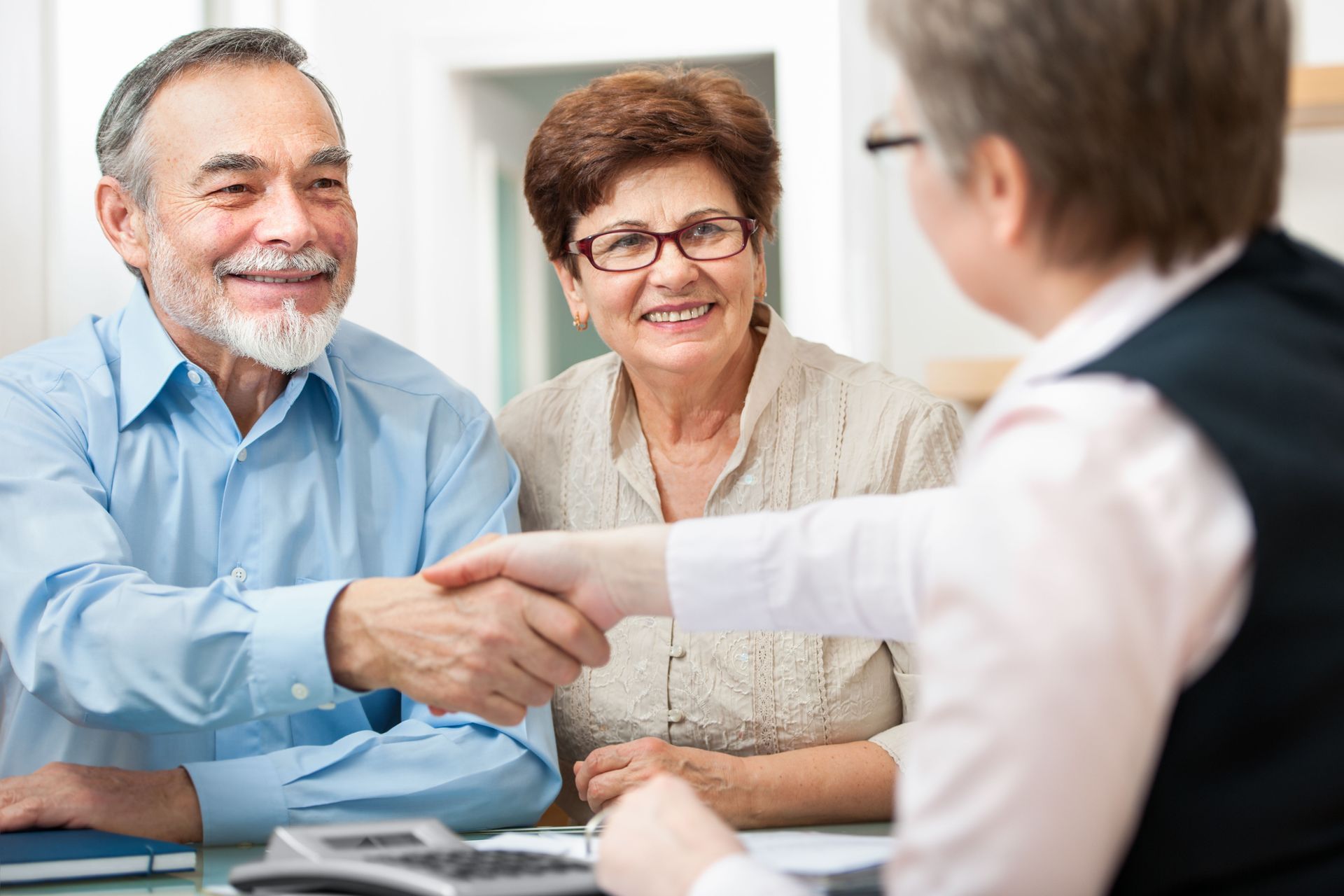 A person in a professional setting shaking hands with a client while another person looks on and smiles.