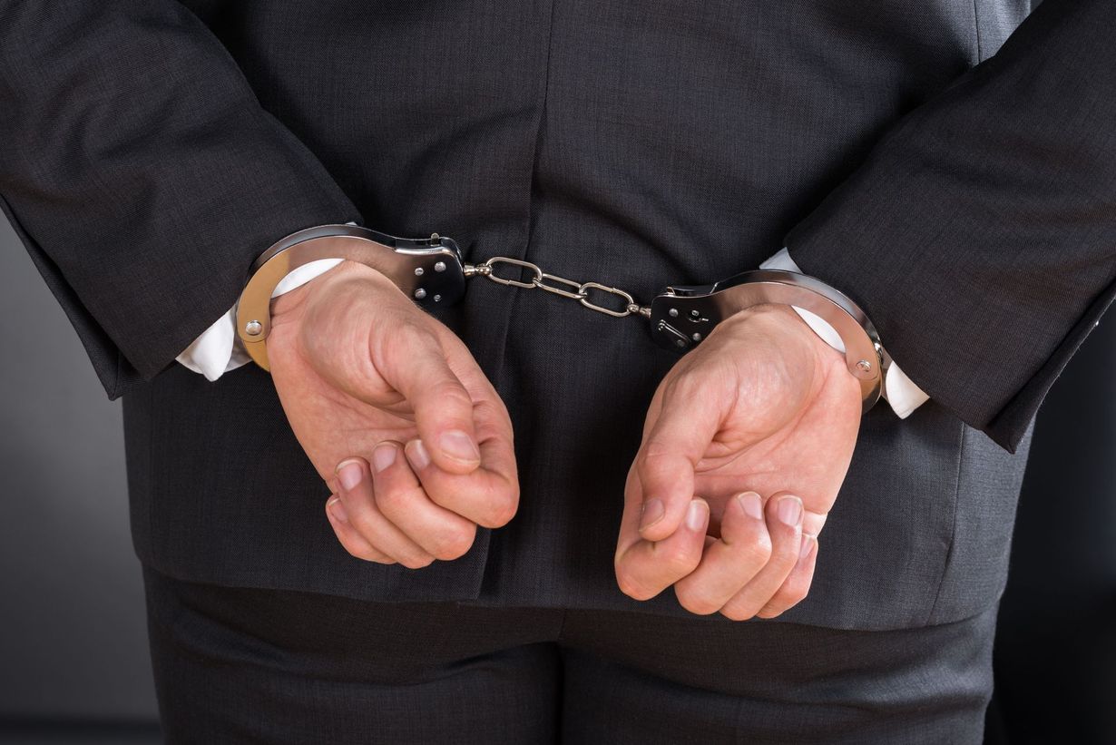 Handcuffed person in a dark suit, seen from behind with hands held behind their back.