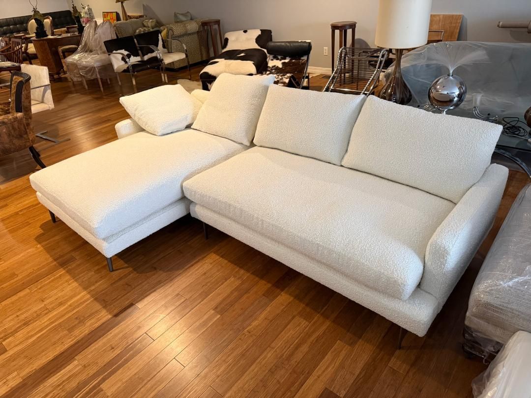 A white, textured fabric sectional sofa with a left-side chaise sits on a hardwood floor in a furniture showroom.