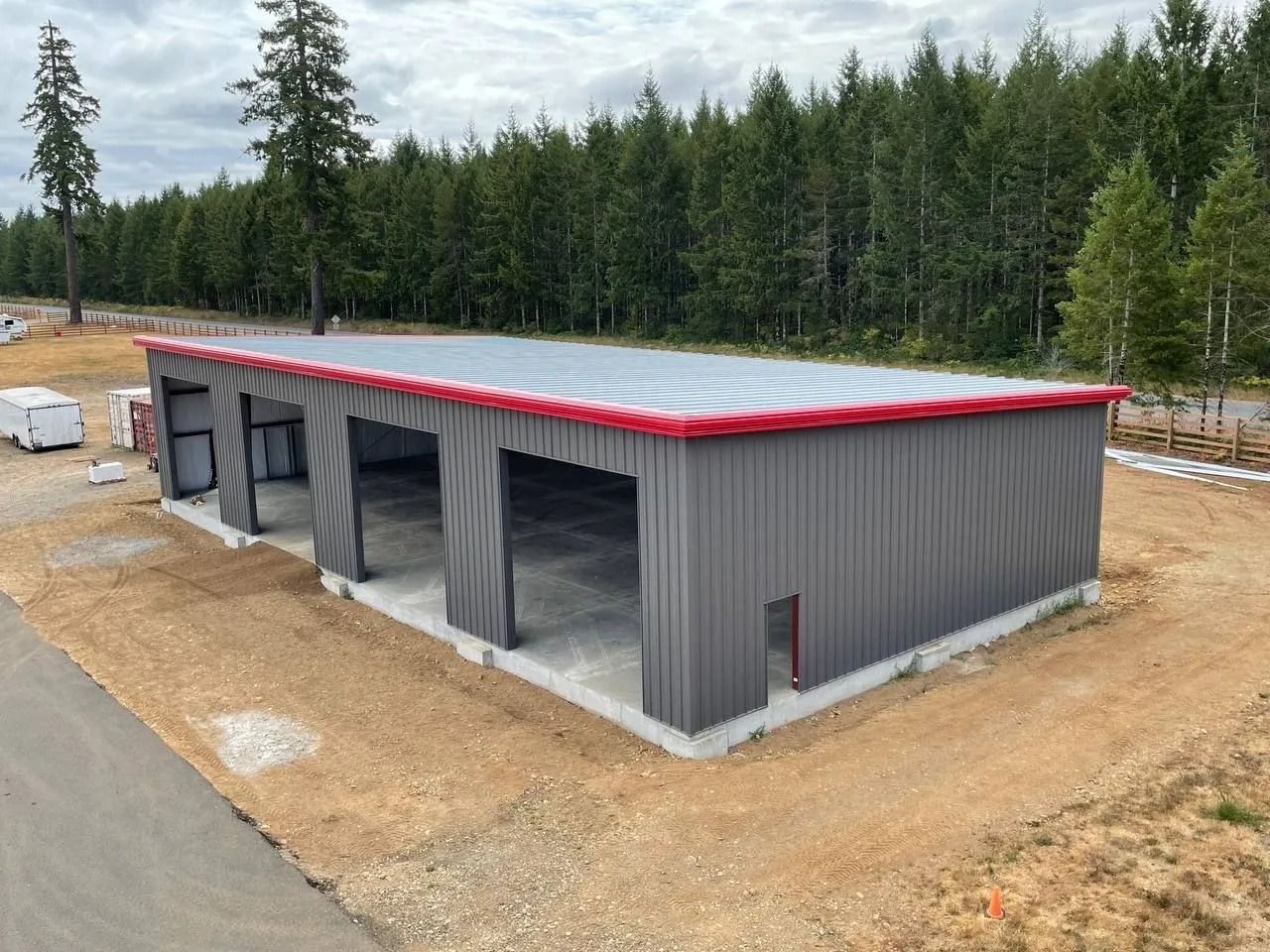 Gray metal building with three bays, red trim, and concrete foundation in a rural setting.