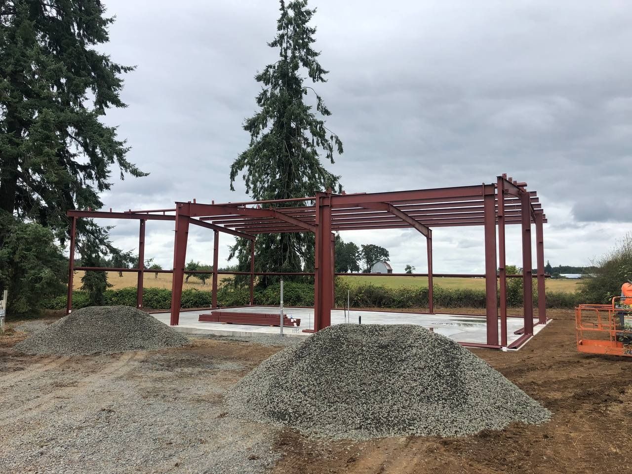 Construction site: steel frame building with piles of gravel and concrete foundation.