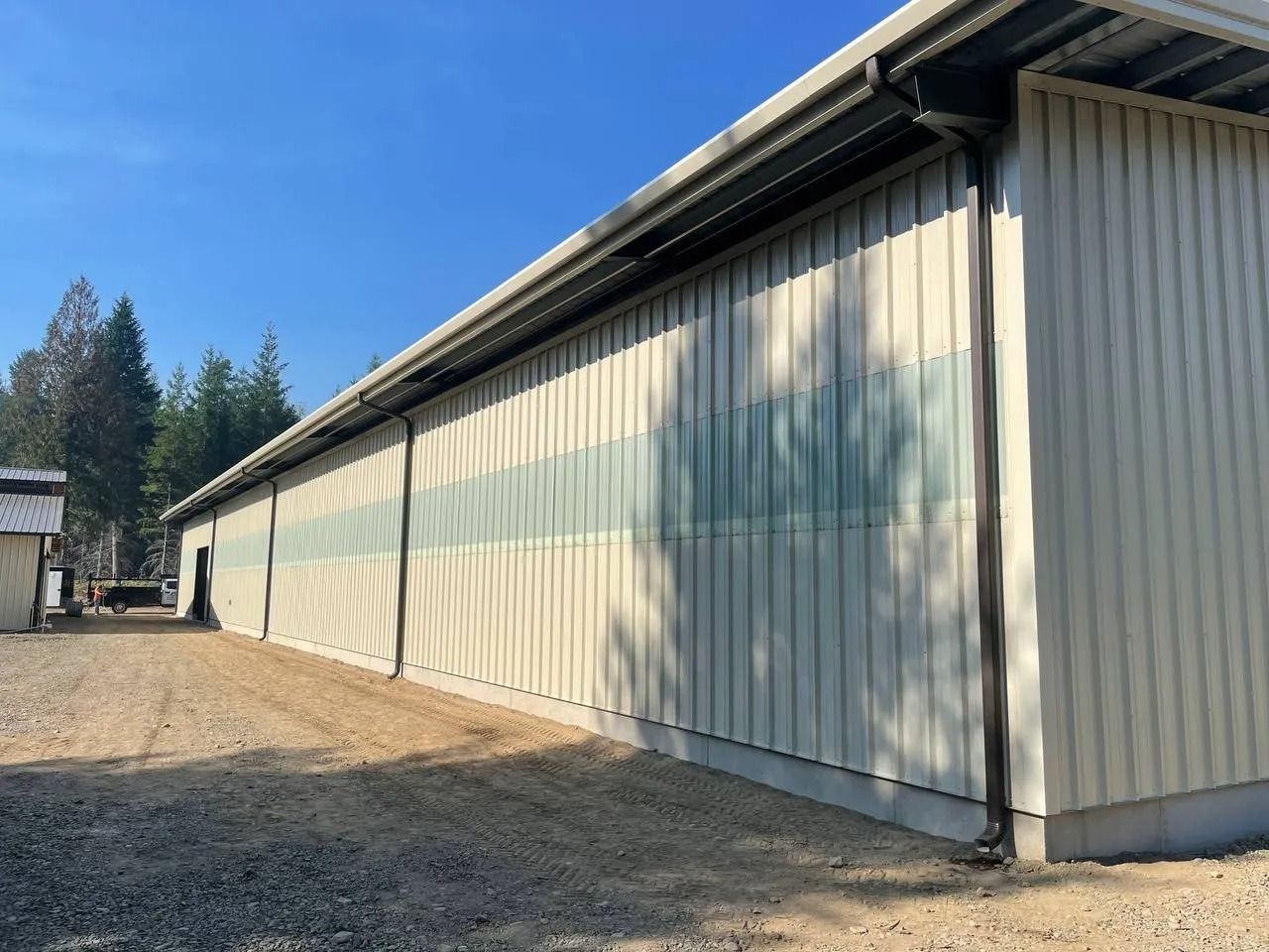 Tan building with vertical siding, green accents, and dark gutters on a gravel lot under a blue sky.