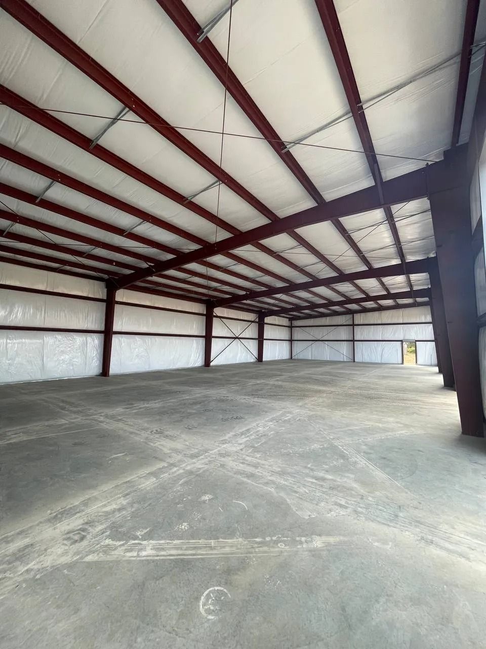 Empty, open-plan metal warehouse interior with concrete floor, red beams, and white ceiling panels.