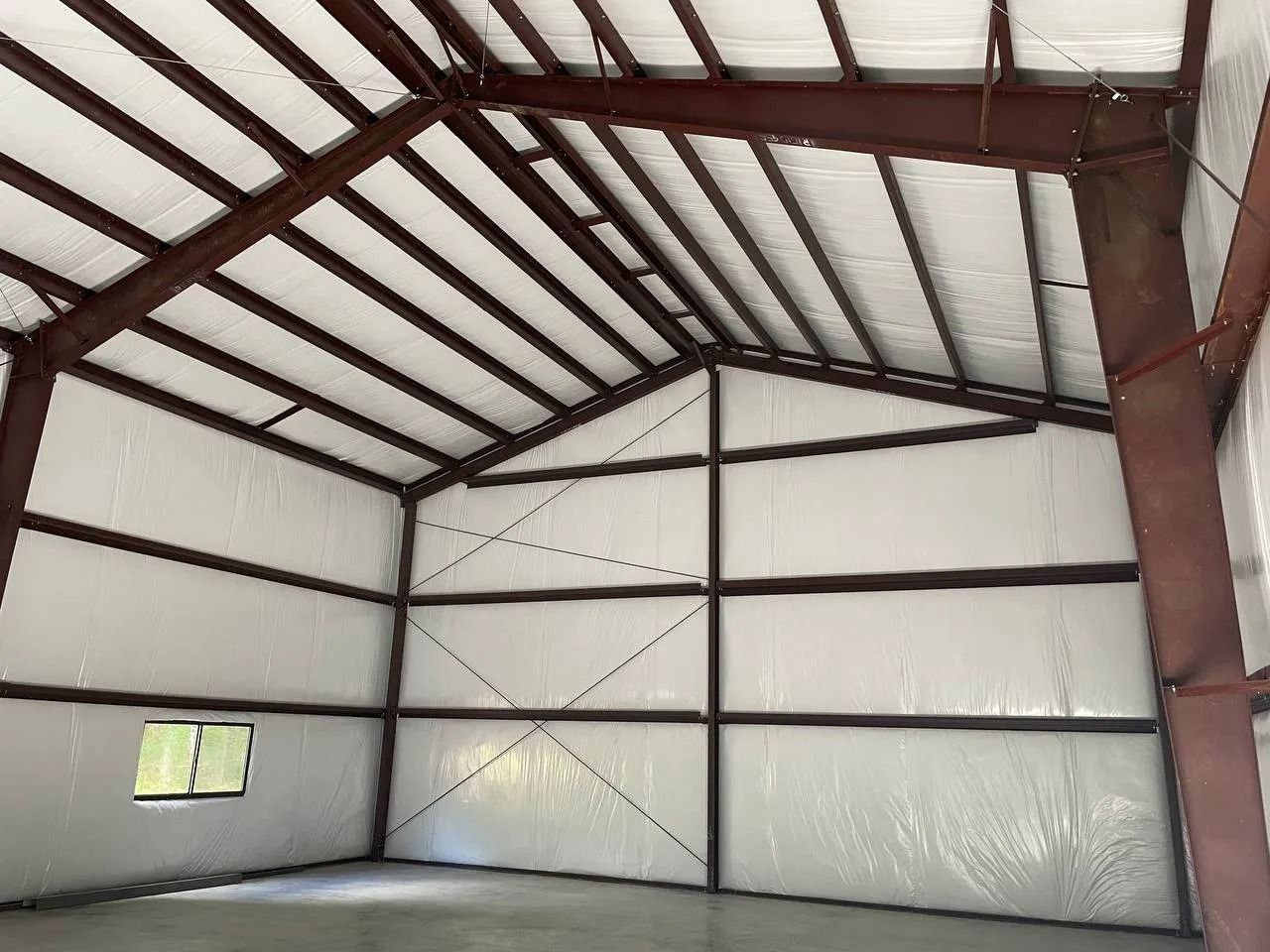 Interior of a metal-framed building with white insulation. The floor is concrete.