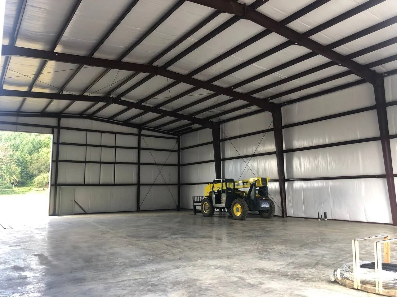 Inside a large metal barn: a tractor-like vehicle is parked. The space has a concrete floor and white insulated walls.