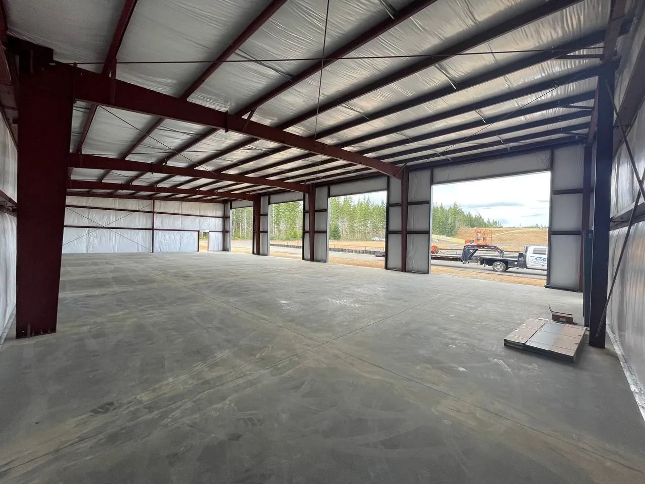 Interior of a large, empty metal building with open garage door bays, concrete floor, and visible steel beams.