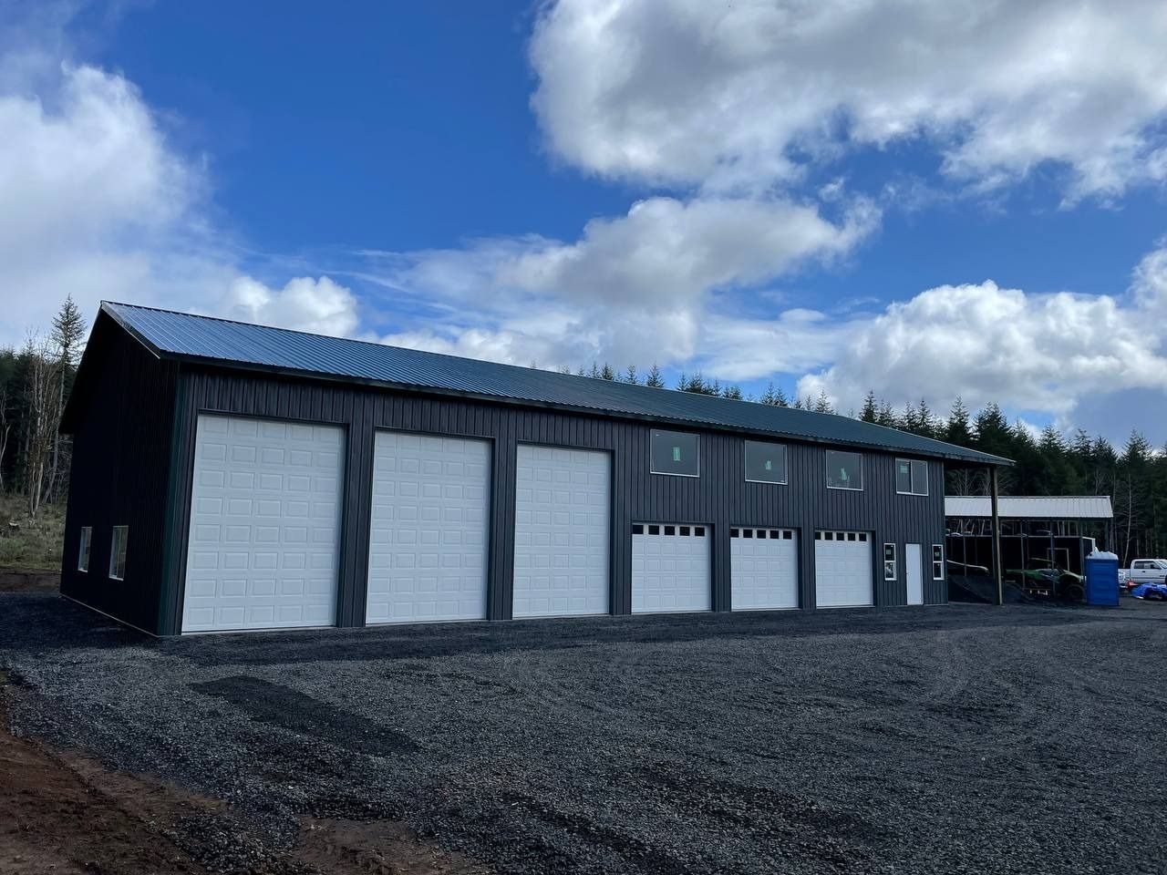 Black metal building with white garage doors under a blue sky.