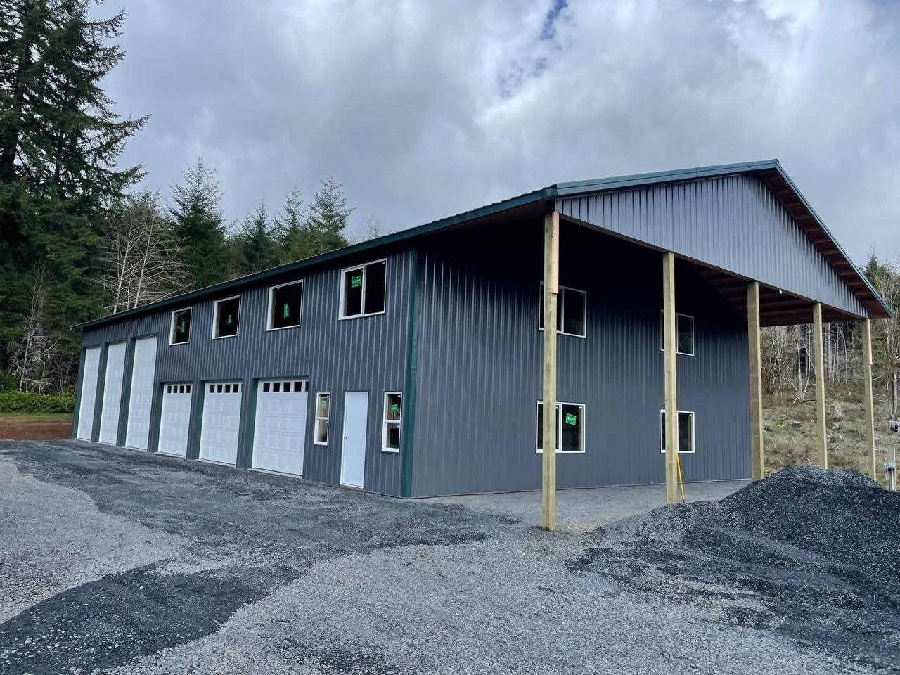 Gray metal building with garage doors, windows, and a covered porch in a gravel area.