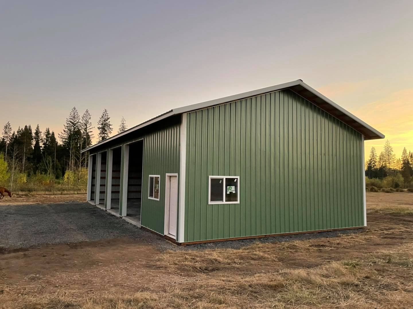 Green metal building with white trim, set against a sunset, with open bays.