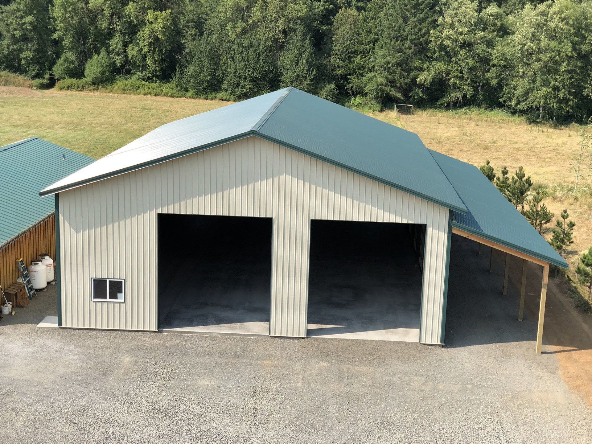 Two-bay light tan garage with a teal roof and gravel driveway, set against a hillside.