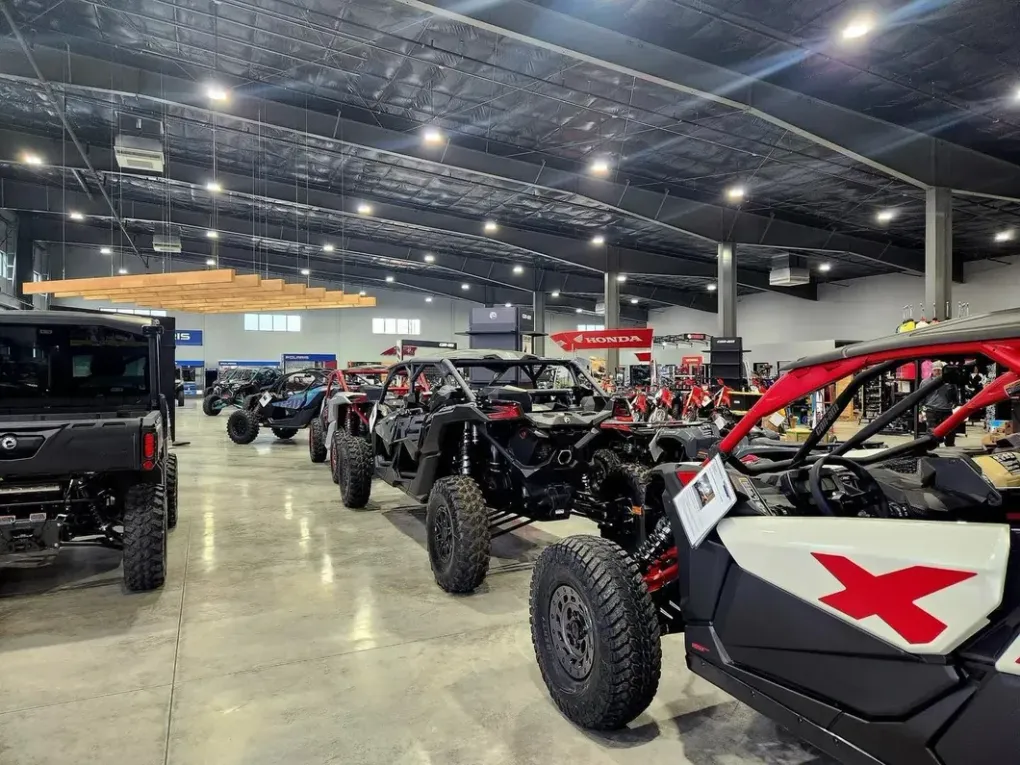 Indoor display of off-road vehicles: UTVs, side-by-sides, and a Jeep, under bright lights.