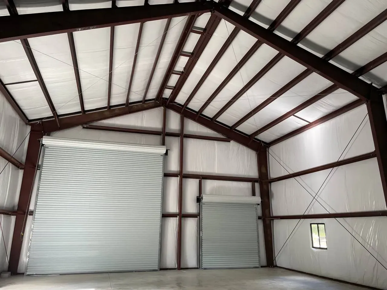 Interior of a steel-framed building with two roll-up doors, metal roof, and white walls.