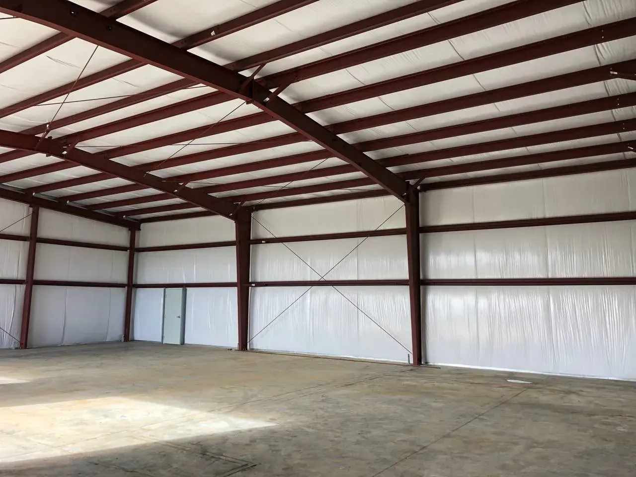 Empty warehouse interior with red steel beams and white insulated walls. Concrete floor.