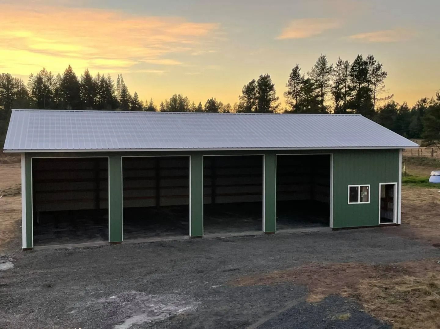 Green metal garage with three bays, a gray roof, and an open doorway.