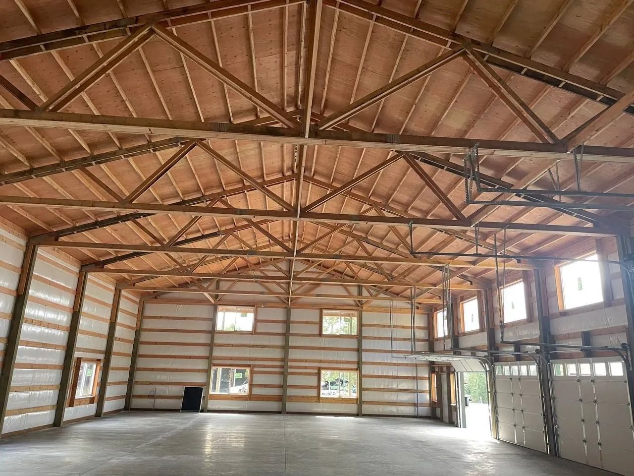 Interior view of a large wood-framed building with high ceilings, concrete floor, and windows.
