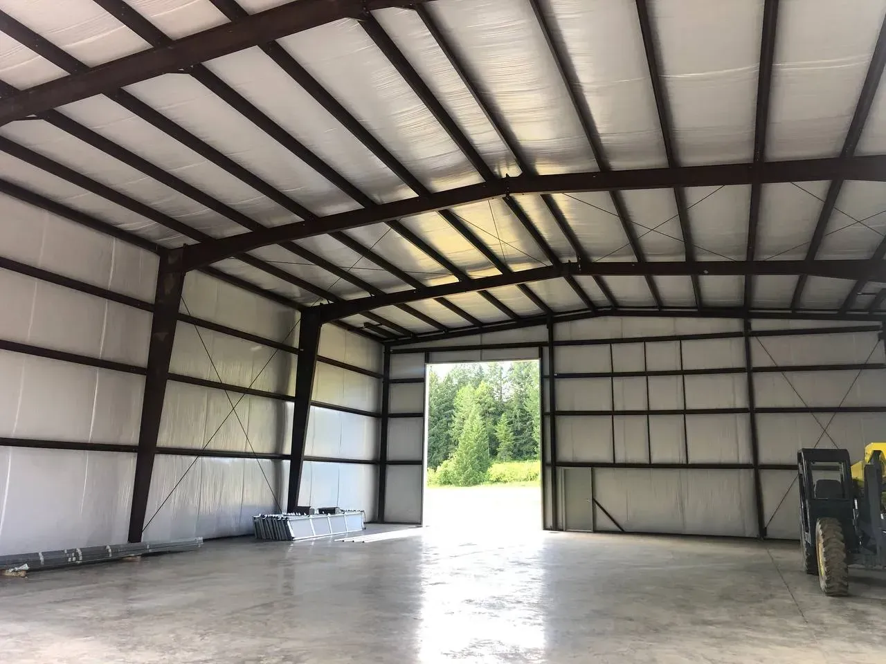 Interior of a large metal building with open door, concrete floor, and brown support beams.