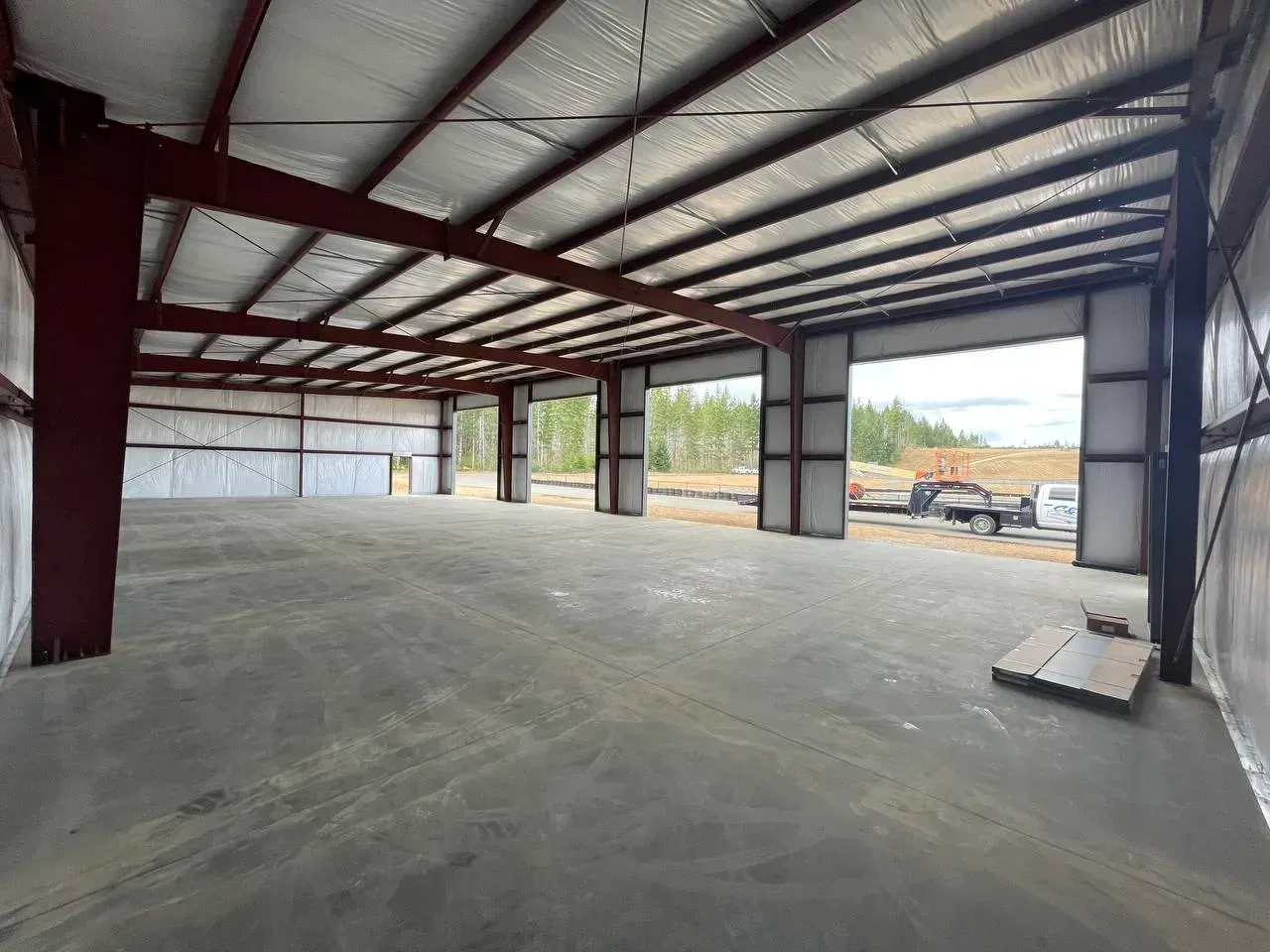 Interior of a steel-framed warehouse with open bays, concrete floor, and silver insulated roof.