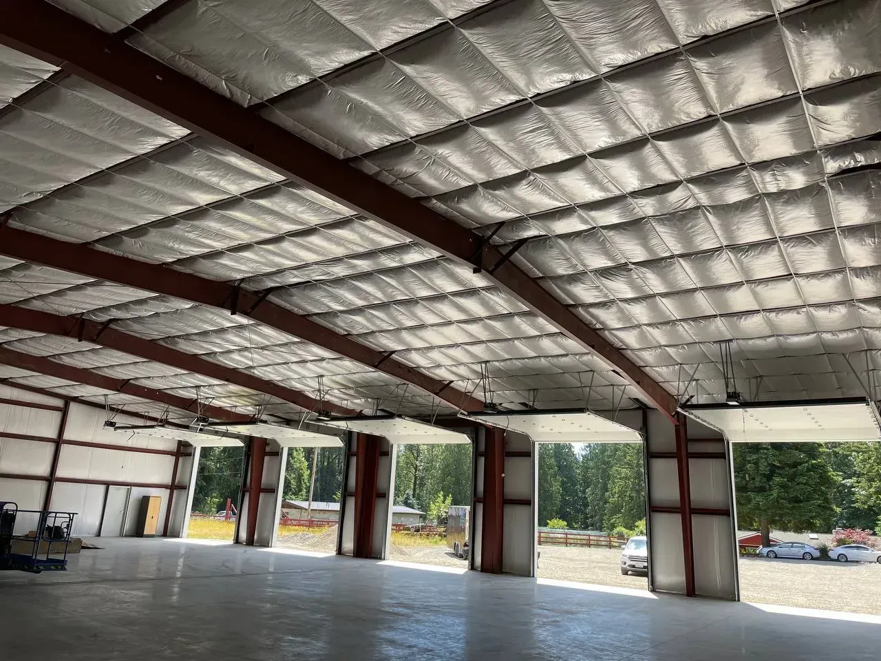 Interior view of a large metal building with an insulated ceiling and open garage doors, concrete floor.