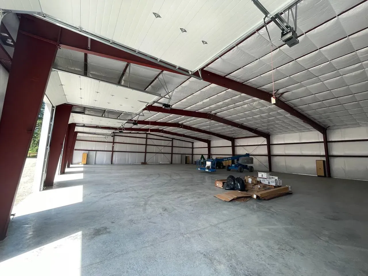 Empty warehouse interior with red support beams and a concrete floor.