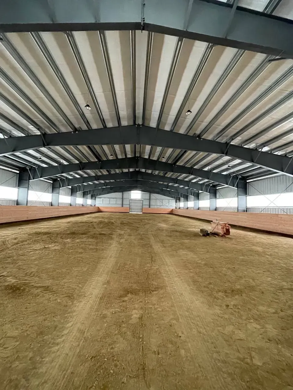 Indoor horse arena with dirt floor, metal beams, and open doorway at far end.