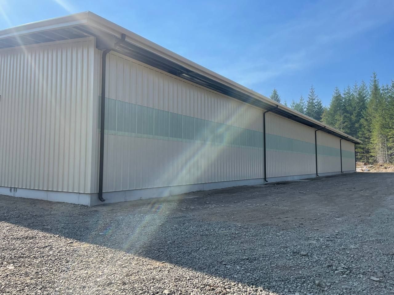 Tan metal building with green stripes on a gravel lot under a blue sky.