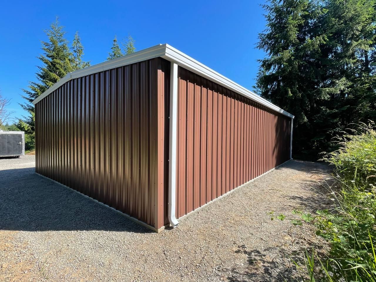 Brown metal storage shed with white trim, set on gravel.