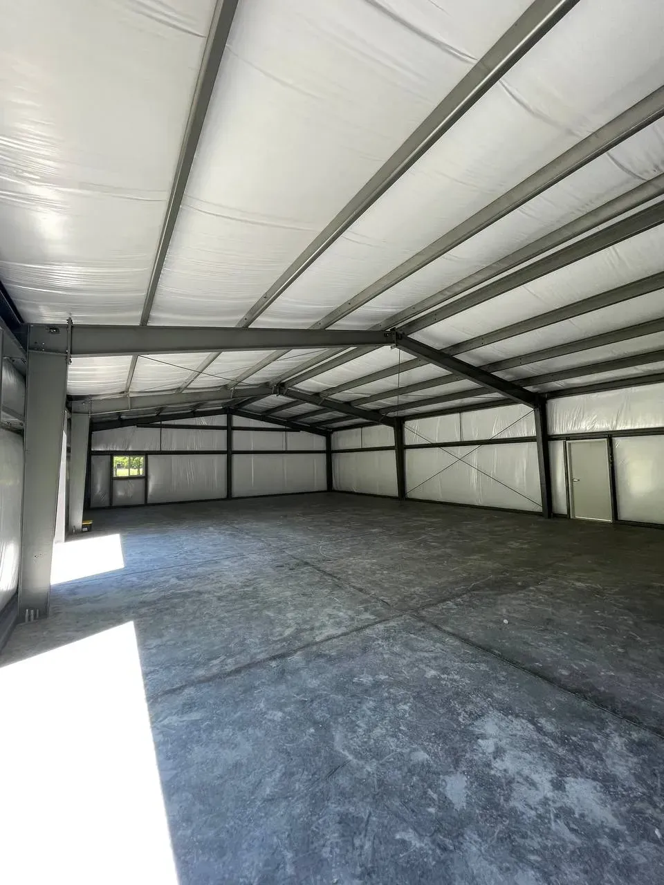 Interior view of an empty metal-framed warehouse with a concrete floor and white ceiling.