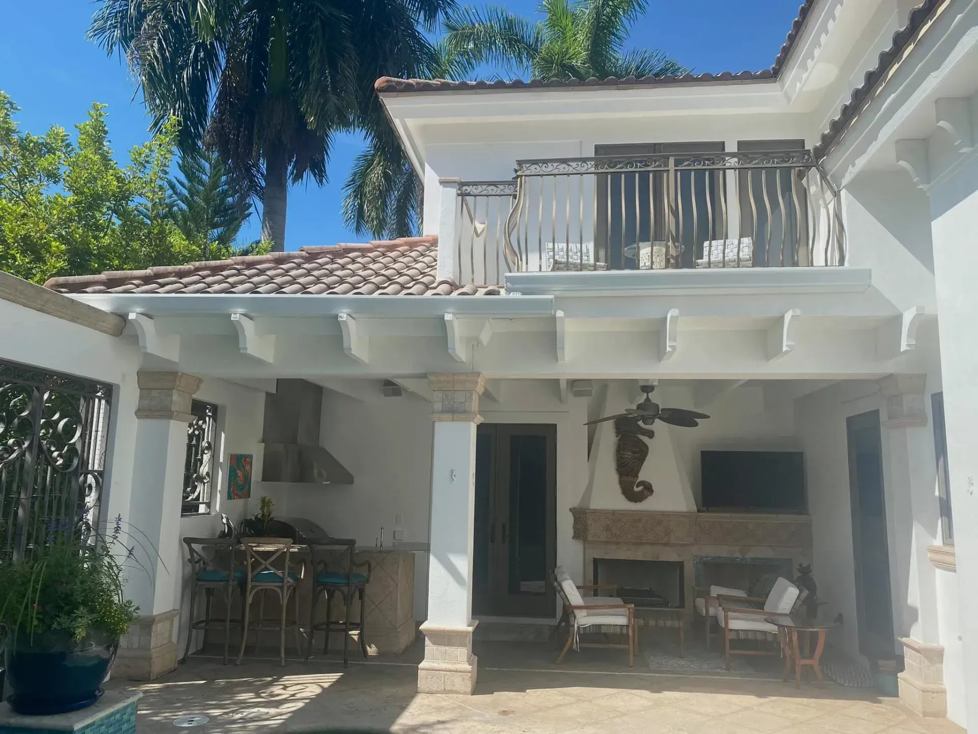 White patio and balcony of a house with outdoor seating under a tiled roof on a sunny day