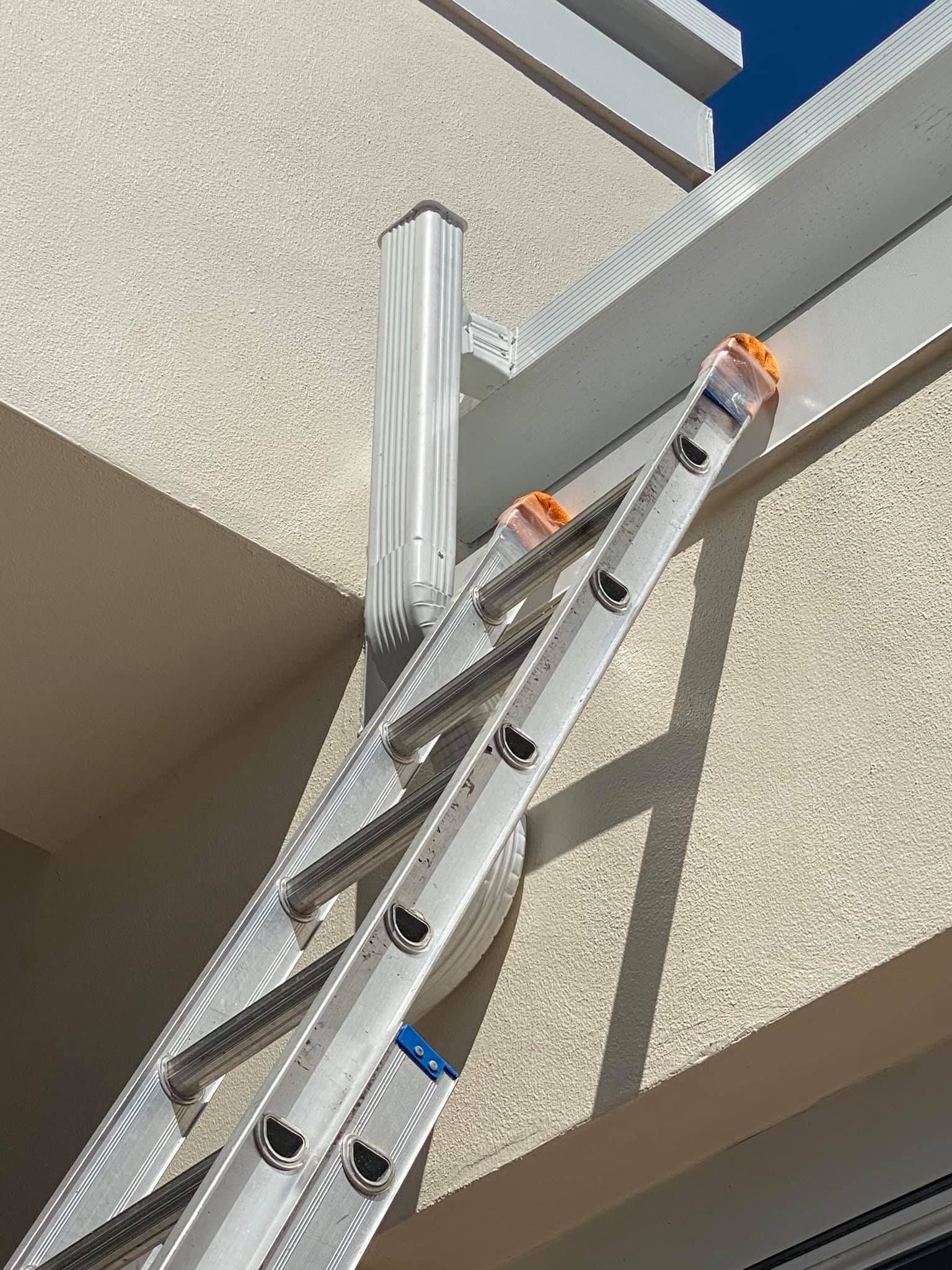 Ladder leaning against a beige building wall near a roof edge and white vent pipe