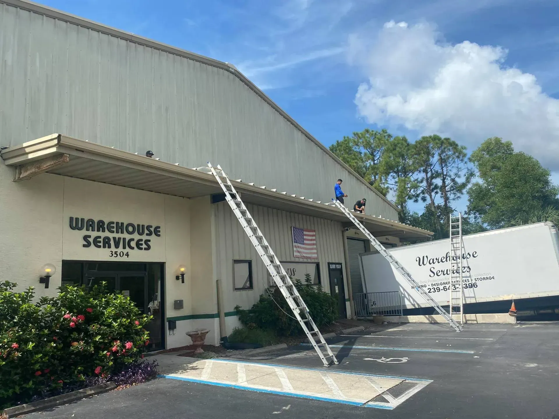 Warehouse Services building with two ladders and blue sky outside a parking lot
