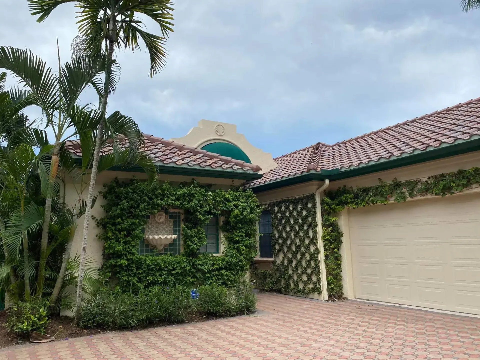 Mediterranean-style house exterior with tiled roof, ivy-covered walls, garage, and palm trees