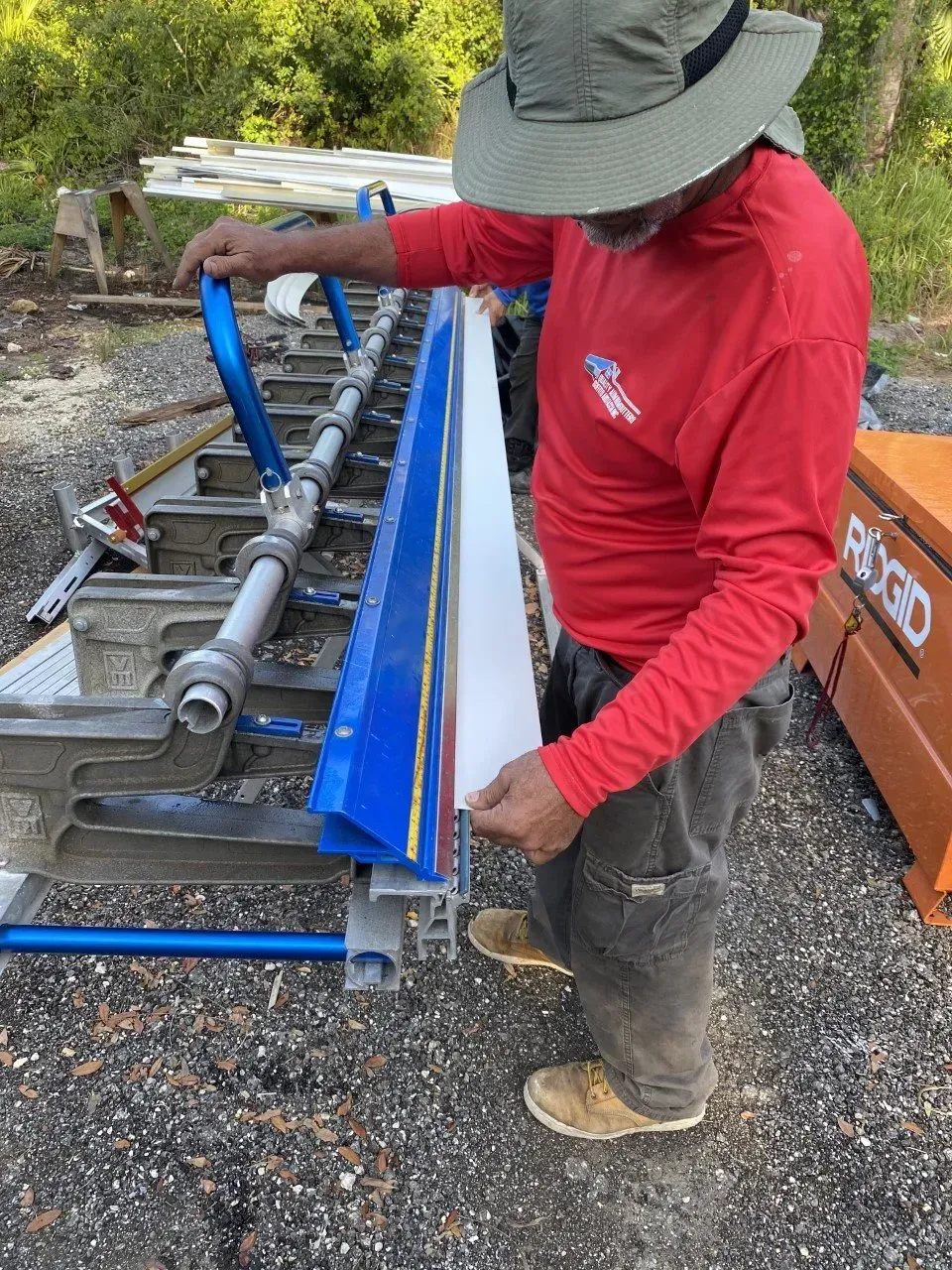 Worker in red shirt adjusting a blue metal machine outdoors.