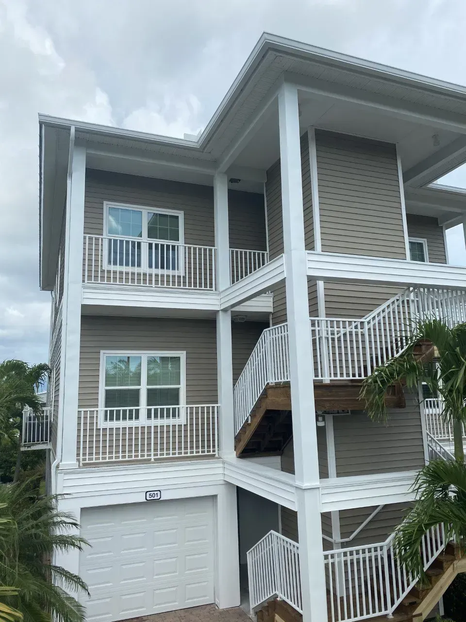 Three-story gray apartment building with white railings and balconies under a cloudy sky