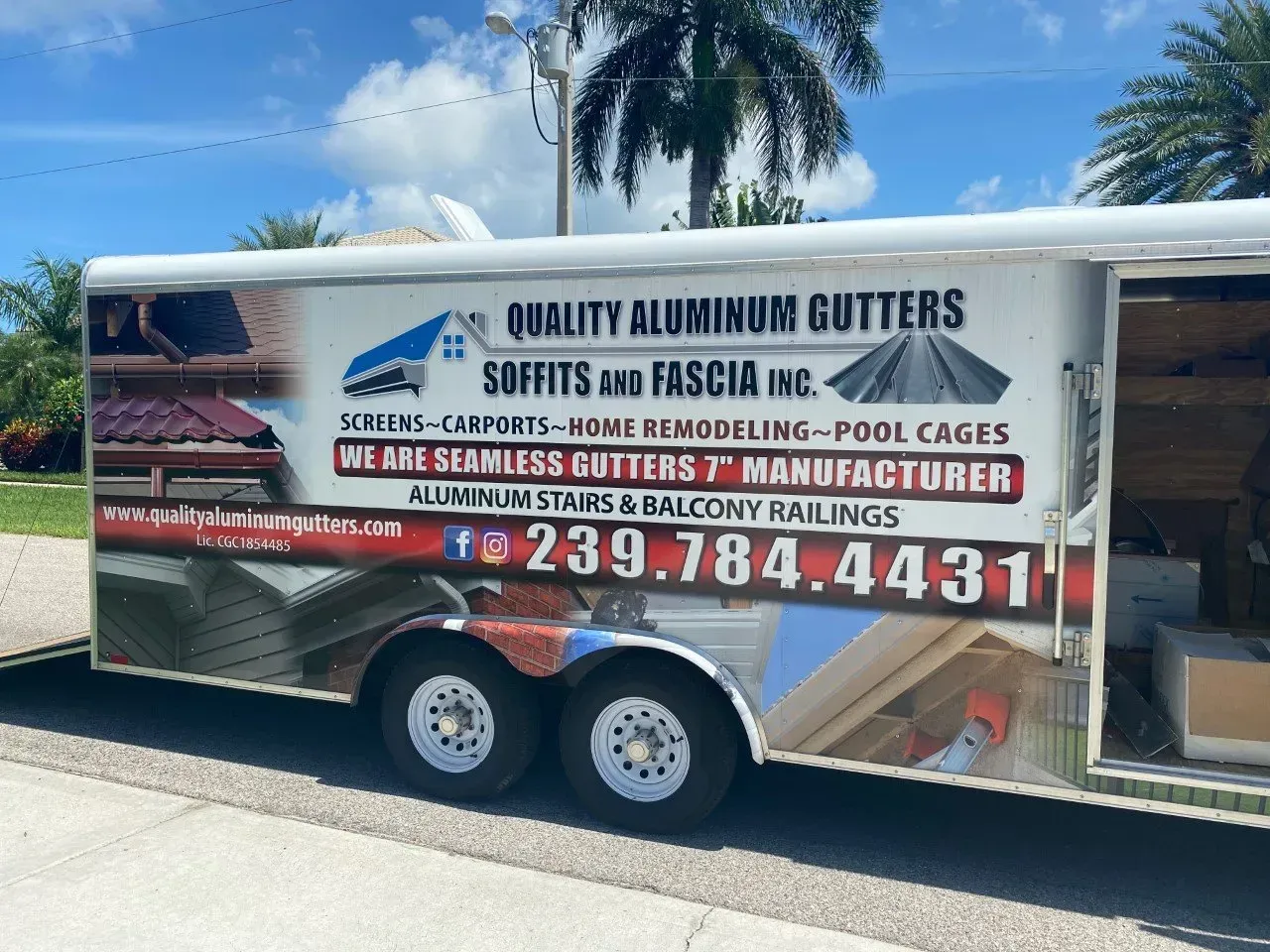 Trailer with “Quality Aluminum Gutters” business ad parked outdoors under blue sky.