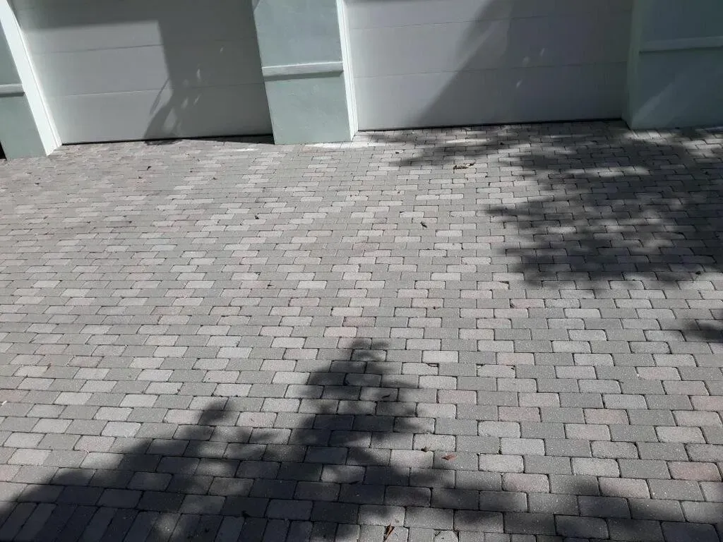 Paved driveway in front of white garage doors, with tree shadows across the bricks.
