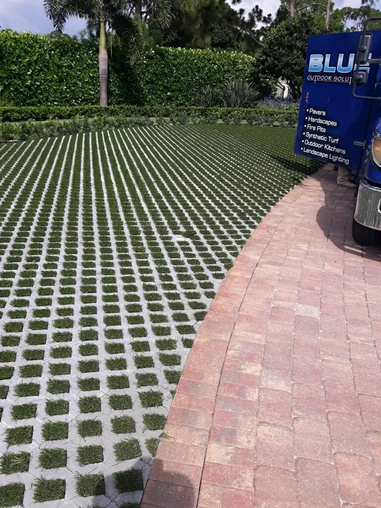 Paved walkway beside a grassy grid lawn and a blue sign in a garden setting