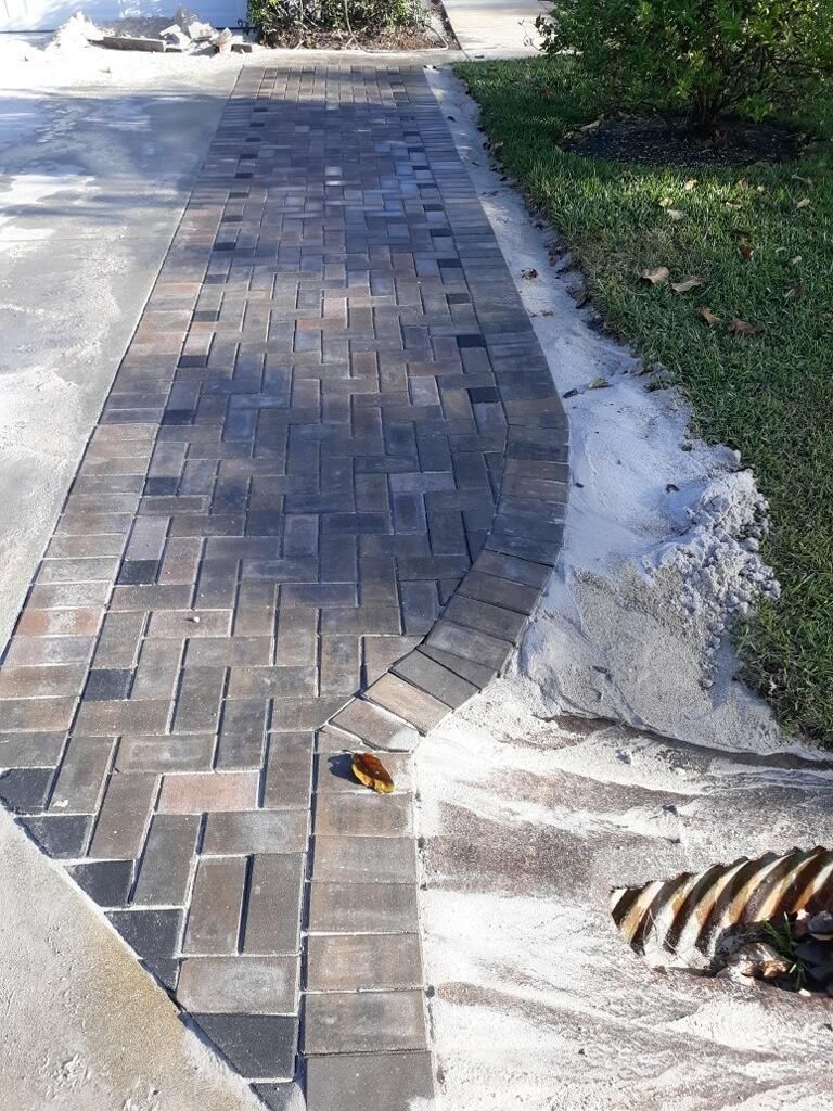 Brick sidewalk curve beside a concrete path and grass, with a small leaf caught in the pavers.