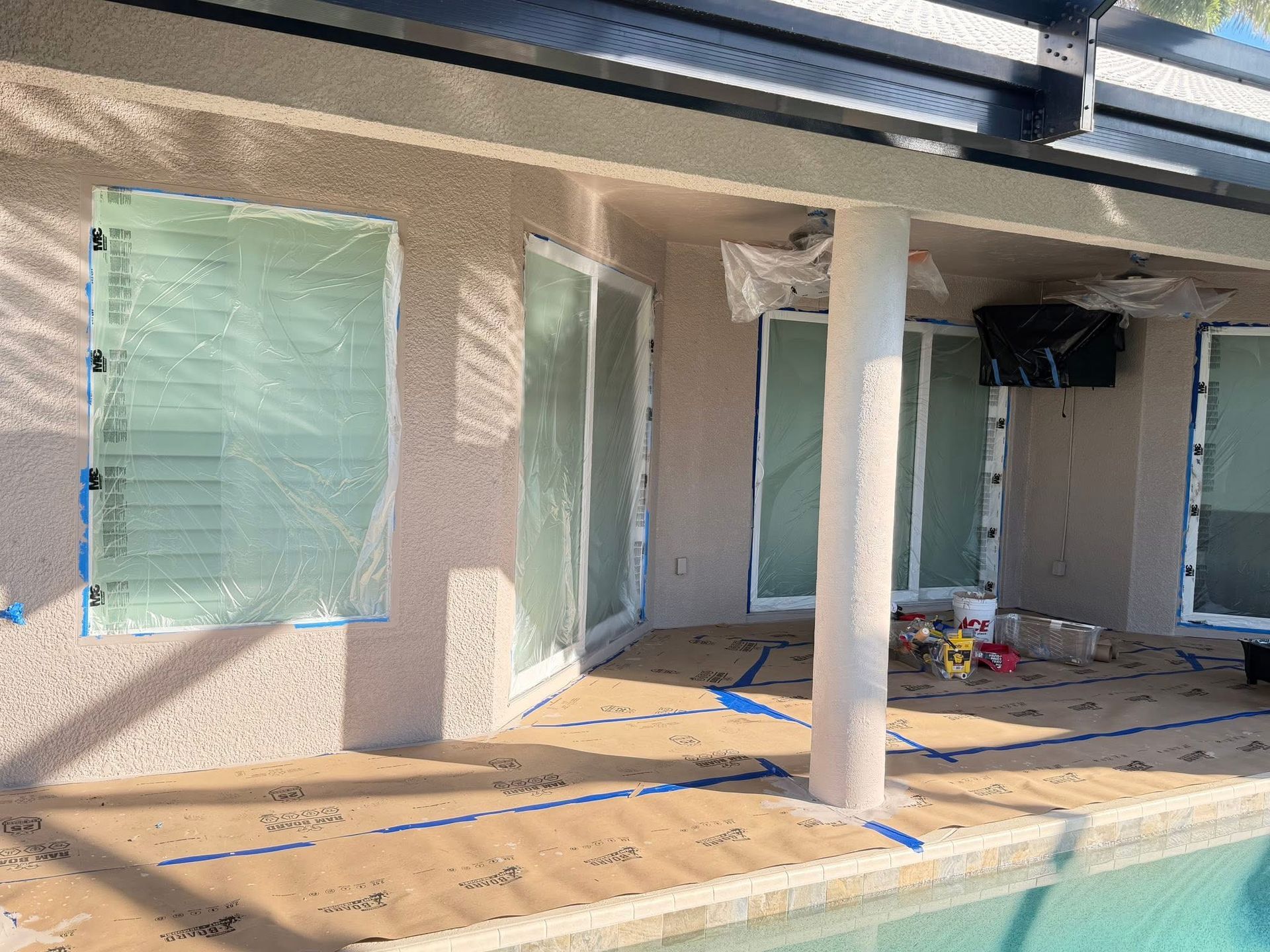 Patio under construction with masked windows, white columns, blue tape, and tools on the floor.