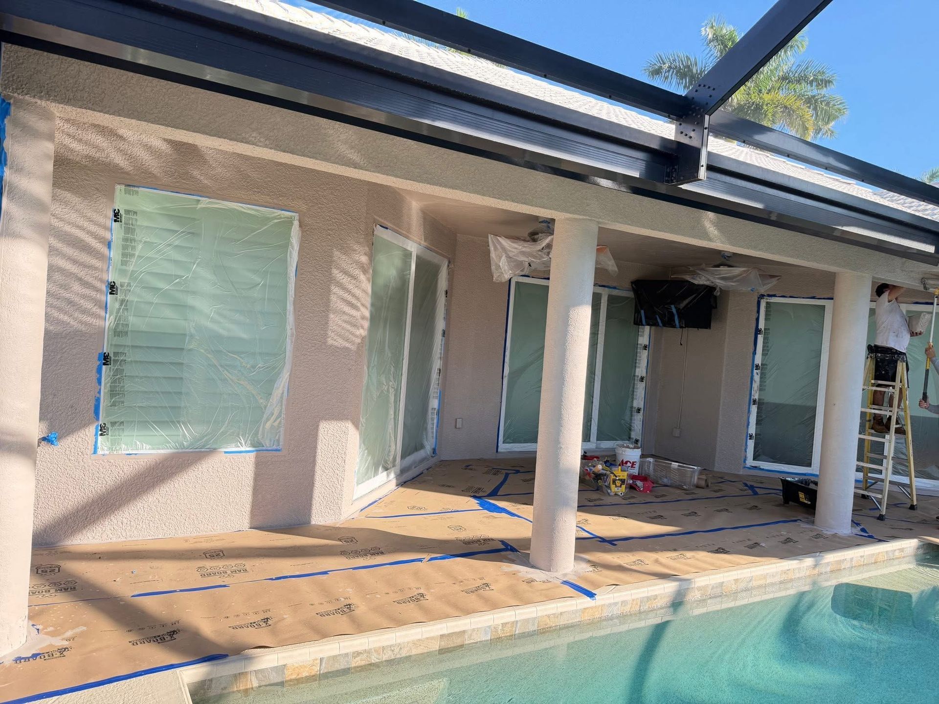 Covered patio by a pool with columns, closed blinds, and renovation materials on the floor.