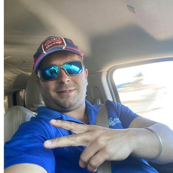 Man in blue shirt and sunglasses making a peace sign inside a car.