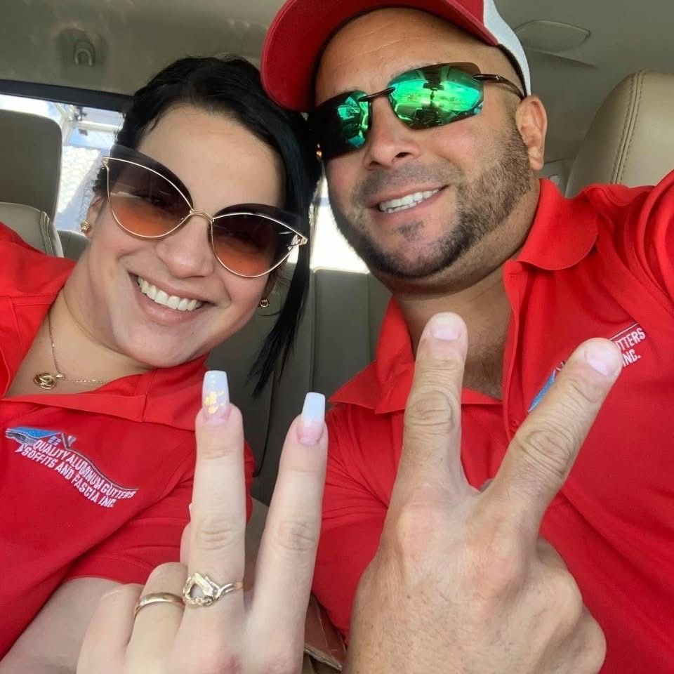 Two people in red shirts smiling in a car, one holding up a peace sign.