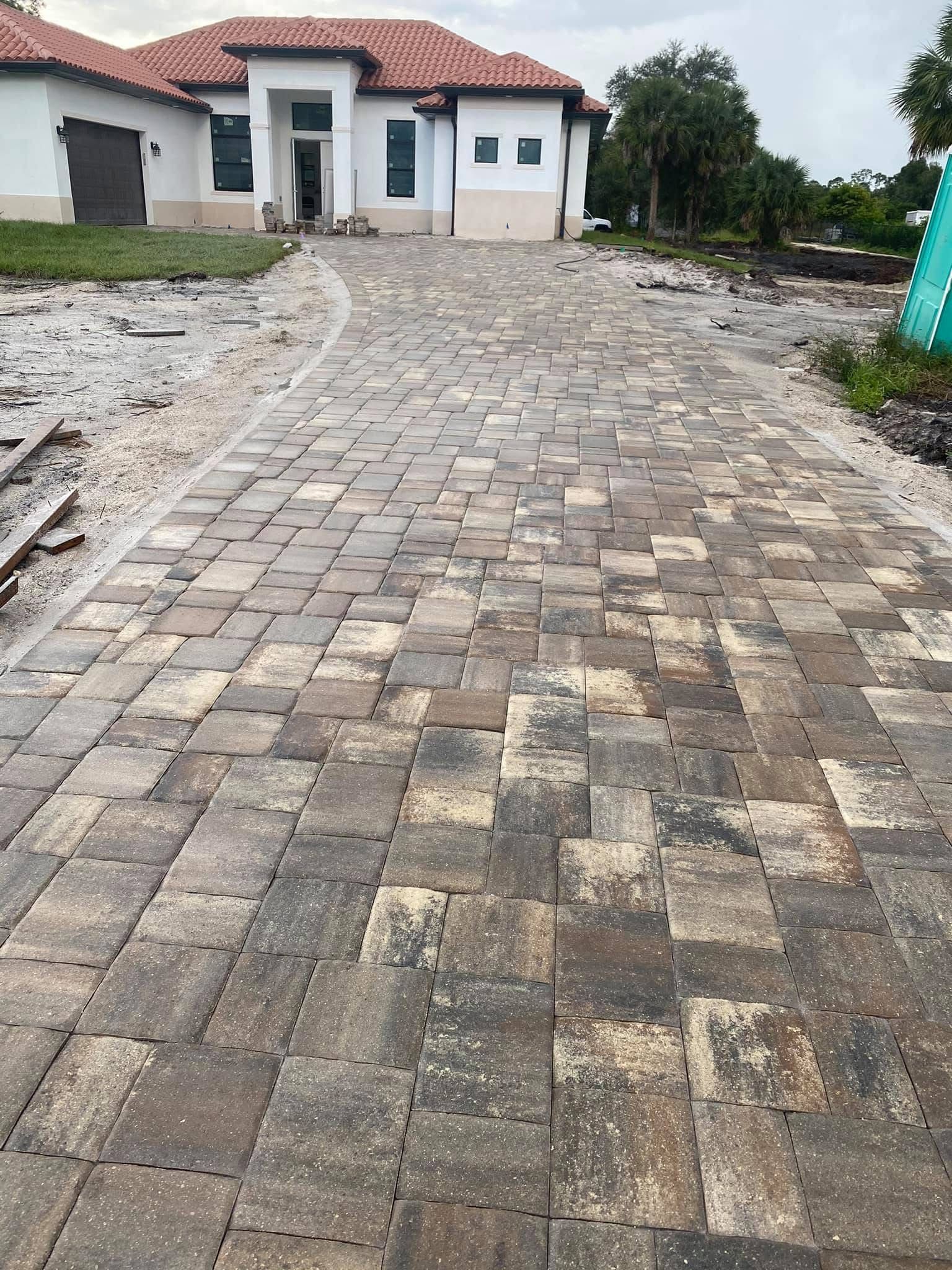 Brick-paved driveway leading to a white house with a red-tiled roof